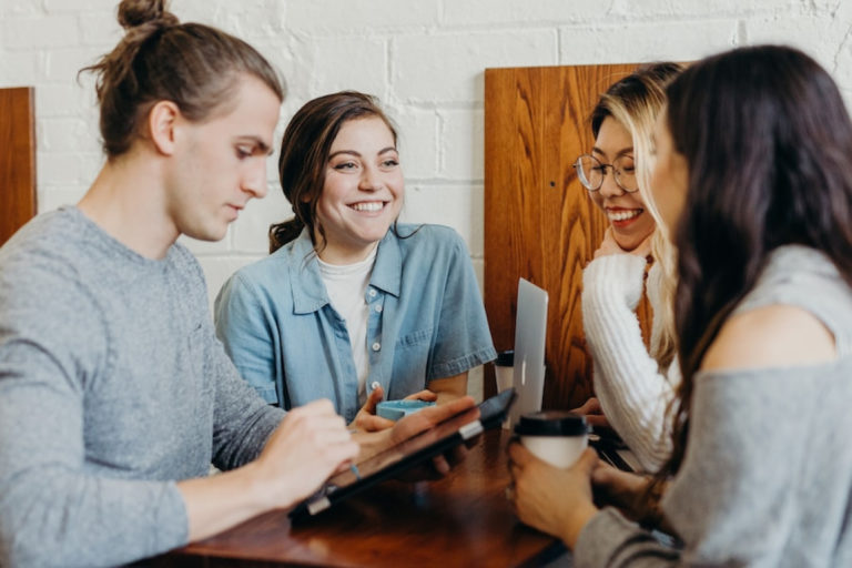 groupe de 4 personnes avec ordinateurs et cafés, discutant à une table