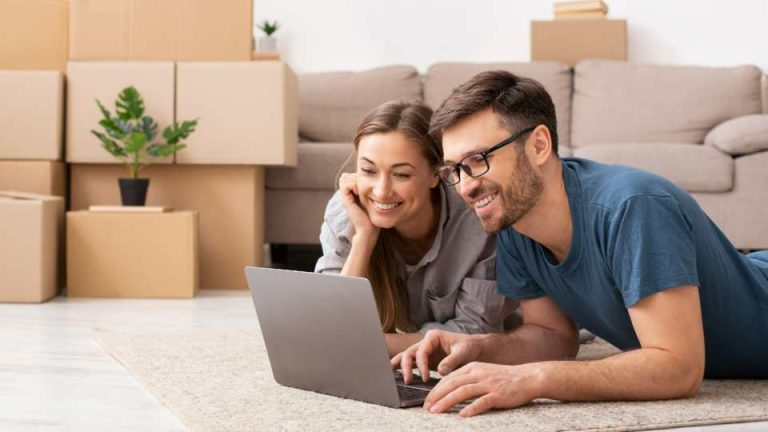 Couple qui consulte un ordinateur avec des cartons derrières eux
